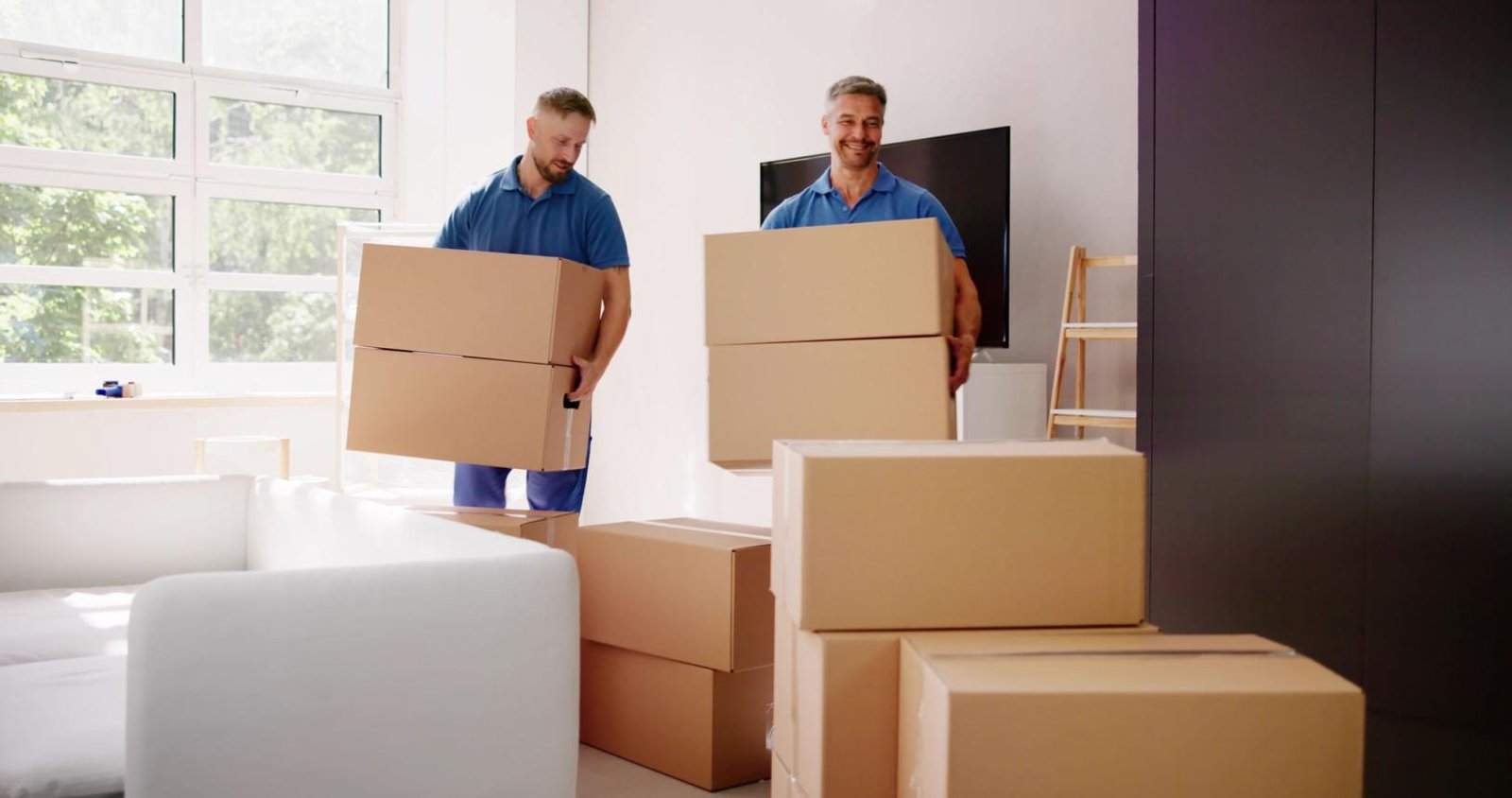 Zwei Mitarbeiter tragen Kartons in einem Wohnraum.